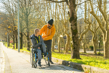 Man pushing the wheelchair of disabled friend along a park