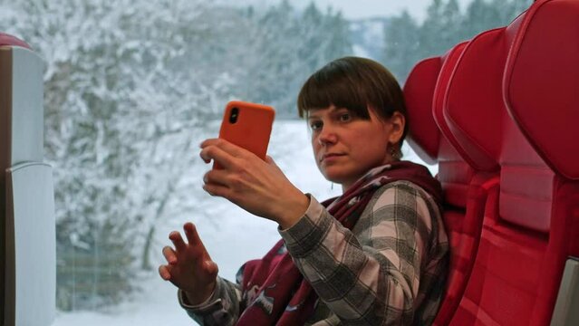 Woman takes a selfie against a window with a snowy landscape. Woman takes a photo of herself while sitting inside a train. The girl films herself on video in transport