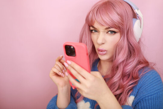 Female model with pink hair taking pictures or recording video on smartphone, listening to music on headphones.