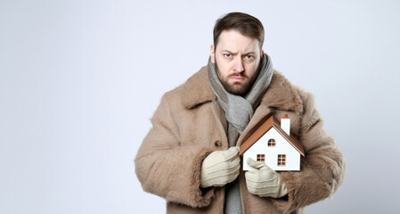 Obraz premium Man in fur coat with house model on grey background. Mortgage concept