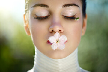 A large portrait of a very beautiful girl with a spring flower on her lips. Perfect spring makeup.A...