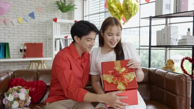 Excited young asian woman opening gift box receiving good unexpected present from husband at home, loving generous boyfriend making romantic surprise to attractive girlfriend on Valentines day