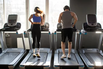 Papier Peint photo Lavable Fitness Back view of active young couple running on treadmills, man and woman performing cardio workout in gym. Families practicing self-care