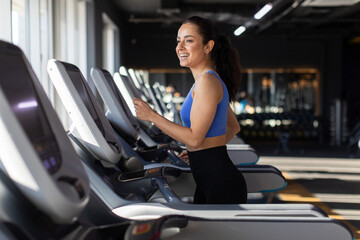 Fototapeta na wymiar Happy young european woman running on treadmill in modern gym, smiling and radiating positivity, enjoying morning fitness routine