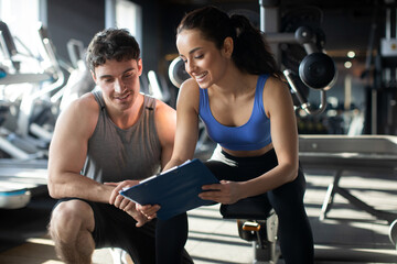 Female personal trainer and her male client discussing nutrition or training plan on clipboard,...