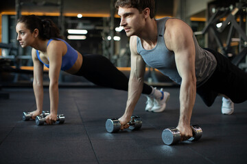 Fototapeta na wymiar Sporty young caucasian couple doing plank or push-ups on weights, working out together in modern dark gym, closeup. Fitness, sports concept