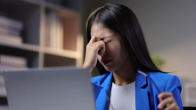 Serious Asian businesswoman stressed with overtime work. Myopia woman working with laptop in office.