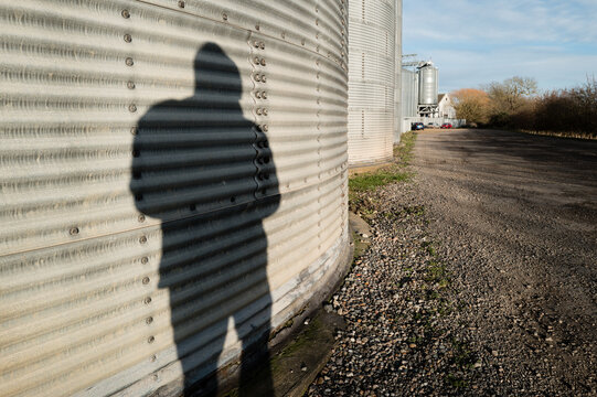 Concept image of a dark shadow of a would-be thief look to entry a factory installation. Th factory houses agricultural grains in silos.