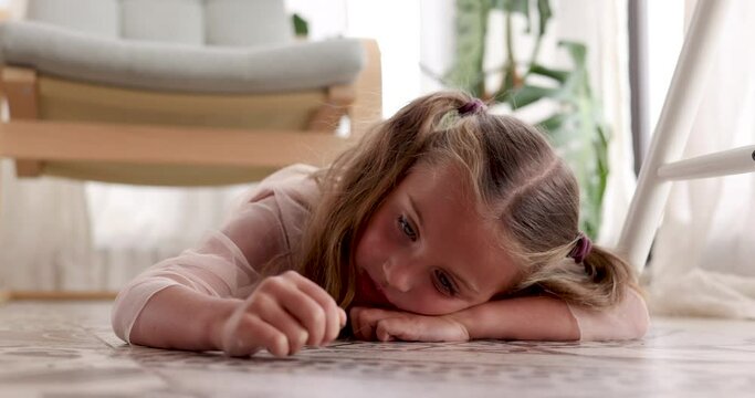 Sad girl at floor in room. Unhappy face of girl. Five year old child little girl is bored lying on the floor running her hand along. Sad lazy kid Preschool education concept. Person loneliness at home