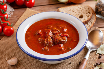 Pork goulash meat on plate, garlic, onion, tablecloth in the background - typical Czech food