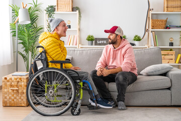 Disabled man in wheelchair and friends chatting relaxed at home