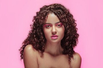 Extreme close-up of a young woman with pink makeup, curly hair, and a pink background