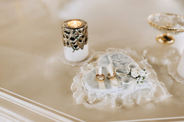 Obraz na płótnie Canvas Wedding accessories, ceremony details. Gold rings lie on a heart embroidered from fabric, a boutonniere of flowers, with a candle in a candlestick.