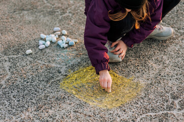 A diligent girl, a child draws a drawing with colored chalk on the asphalt with his hand on the street in a park in Ukraine. Close-up photography, design, childhood concept.