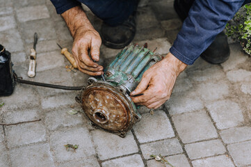 Elderly male professional worker, electrician, electromechanic repairs an old rusty electric motor...