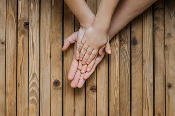 Family, mother, children - boy and girl holding hands together on a wooden background showing care. Close-up photography, love concept, copy space, top view.