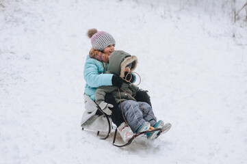 A little boy with a girl sister, happy children, family sledding, going down a hill in the snow in...