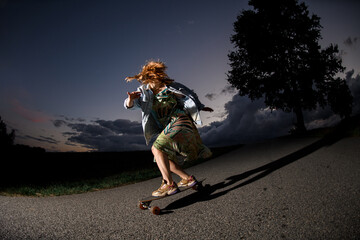 Fototapeta premium Young girl is riding a longboard on the road, her arms are out to the sides and her hair is flying in different directions