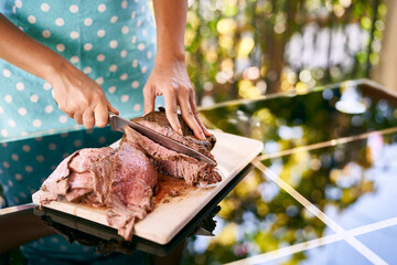 Chef cuts a juicy roast beef with a knife on a cutting board on a mirror table