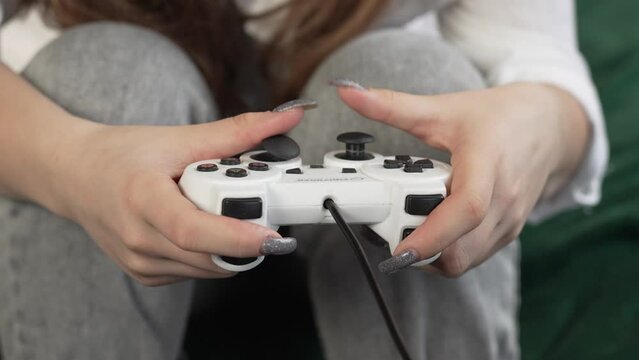 Young girl with painted nails: teenager immersed in console games, cinematic gameplay shot on sofa with joystick close-up