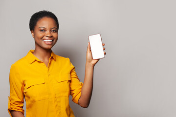 Confident woman showing smartphone with empty blank screen display. Model in yellow shirt with...