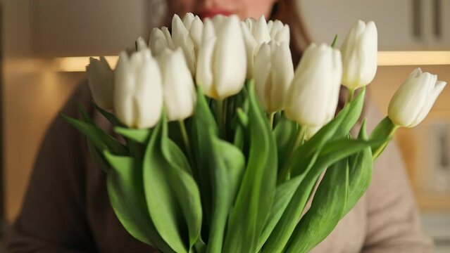 Closeup image of carefree happy 30s woman with tulips flowers for home, close eyes smiling and sniffing beautiful white bouquet. Housewife taking care of coziness in apartment. . High quality FullHD