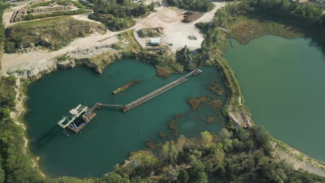 Aerial view of an abandoned quarry. The flooded bottom creates a lake with green waters. An old machinery for stone extraction emerges from the water.