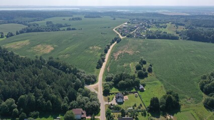 Aerial view from a drone on a country road in the middle of a European village with private houses and plots in summer. A village in the middle of a forest. Sandy road in the countryside.