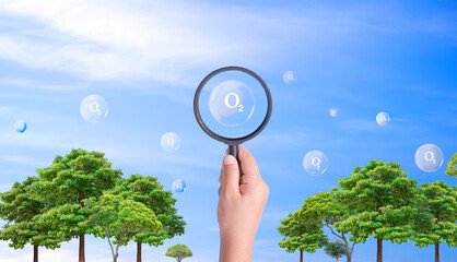 Hand holding magnifying glass with O2 molecular text in many bubbles on the air and green trees in...