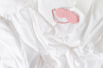 Pink eye mask for sleep on white bedclothes at home, minimal lifestyle aesthetic flat lay photo....