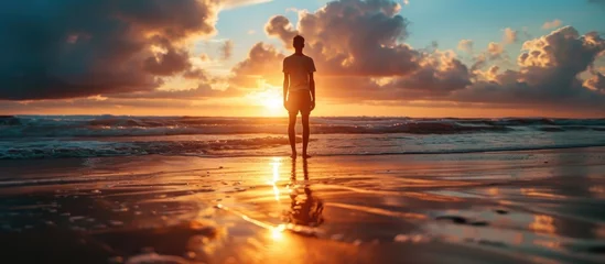 Photo sur Plexiglas Coucher de soleil sur la plage Solitary young man on beach with stunning sunset backdrop.