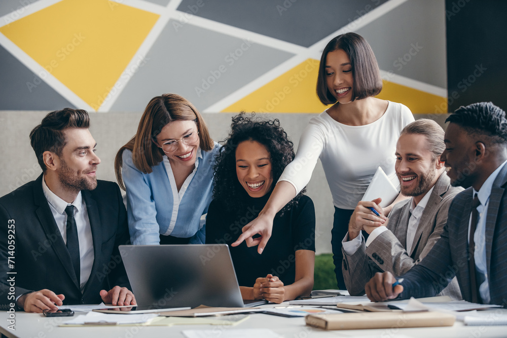 Poster smiling young business team looking at laptop while having group meeting in the office together