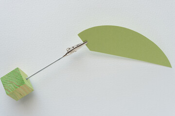 green paper oval segment shape, metallic alligator clip card holder, and green cube on blank paper
