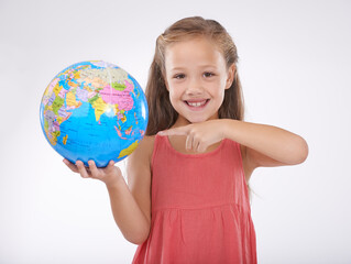 Child, pointing to globe in studio with world, planets and city for education, geography and portrait. Student, girl kid and travel map with smile for earth day support or ecology on white background