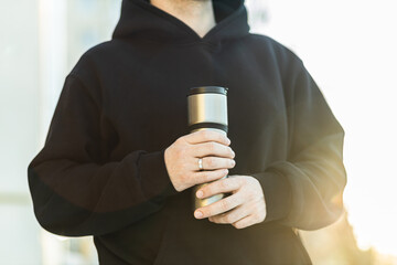 A man holds a thermos mug in his hands. Close-up of thermos in hands. Warming in winter.