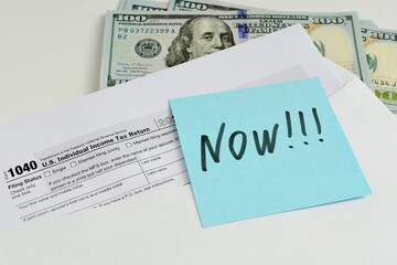 US Tax Form 1040 document in an open envelope and dollar bills on the table. The concept of...