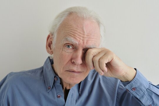 Portrait of a gray-haired elderly crying man wiping away his tears with his hand.