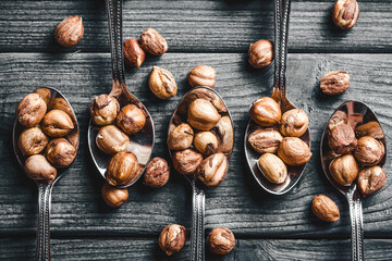 Hazelnuts background. Nuts on spoons. Five silver spoons on gray wood. Wooden table nuts background. Rustic colors healthy snack. Food on wood. Shelled hazlenuts texture.