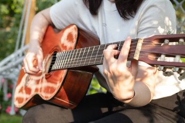 Woman playing acoustic guitar in the garden. Closeup of female hands. - obrazy, fototapety, plakaty
