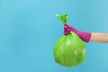 Woman holding plastic bag full of garbage on light blue background, closeup. Space for text