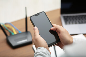Man with smartphone and laptop connecting to internet via Wi-Fi router at wooden table, closeup
