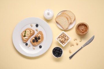 Toasts with tasty nut butter, blueberries and cashews on beige background, flat lay