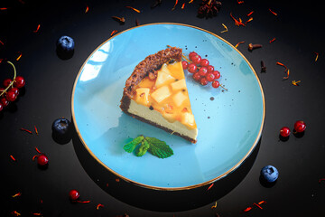 Cheesecake with yellow mango flavoured layer decorated with mint,  blueberries and red currants on black  background, top view.