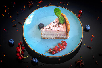 Berry cheesecake decorated with mint, blueberries and red currants on black background, top view.