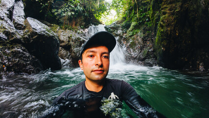 young man swimming in a waterhole of a waterfall in a forest with trees on vacation