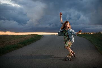 Young girl rides in the middle of the road on her longboard with her arms out to her sides for...