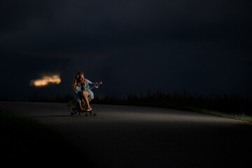 Young girl rides down the road squatting on a longboard and holding on to it with one hand