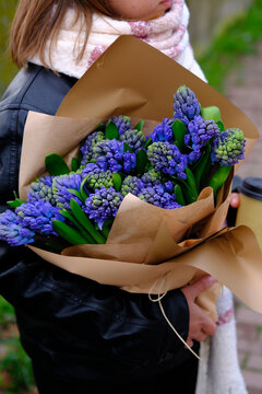 Elinde bir buket mavi sümbül çiçeği ve yaprağını inşaat kâğıdı kornetinde tutan kadın