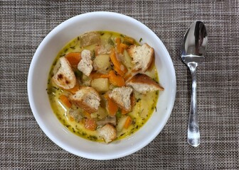 Potato and carrot soup in a white bowl with spoon topped with croutons