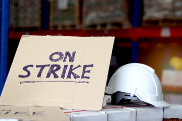 On strike banner placard with white worker helmet at cargo logistic warehouse. Striking worker protesting and do not to work at workplace, symbol of strike concept.